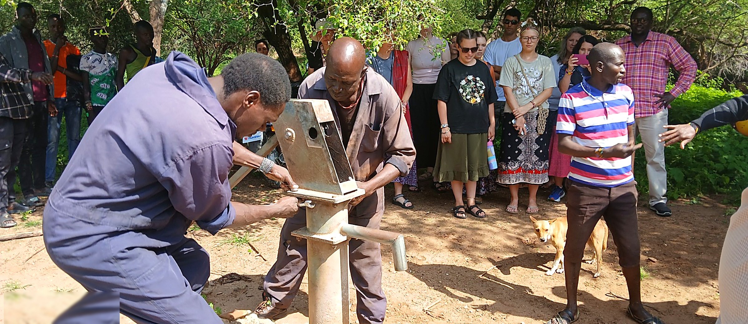 Technicians installing the head of a hand pump on a completed borehole
