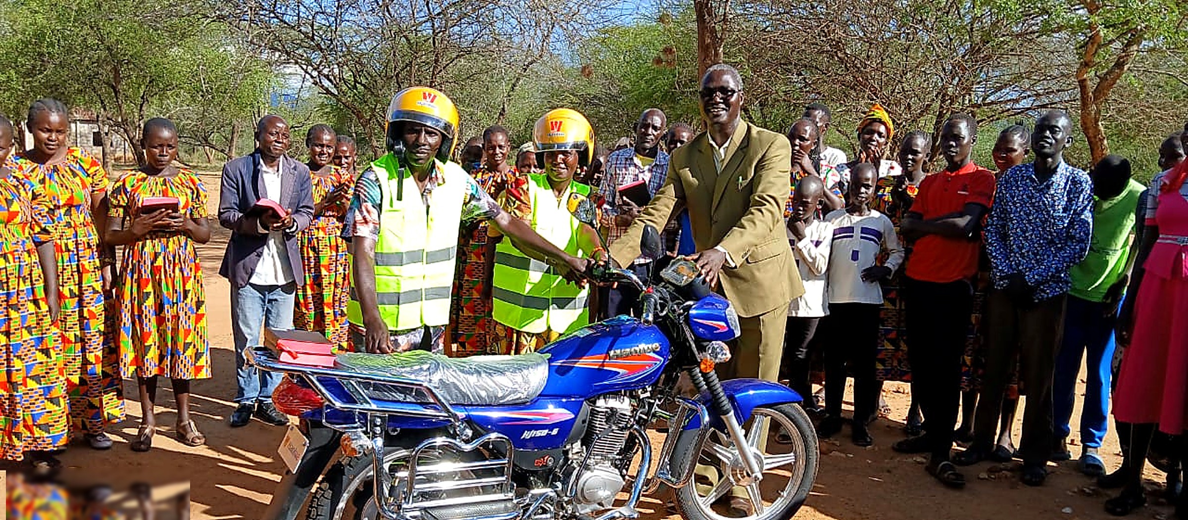 Handover of a motorcycle to field workers surrounded by the community