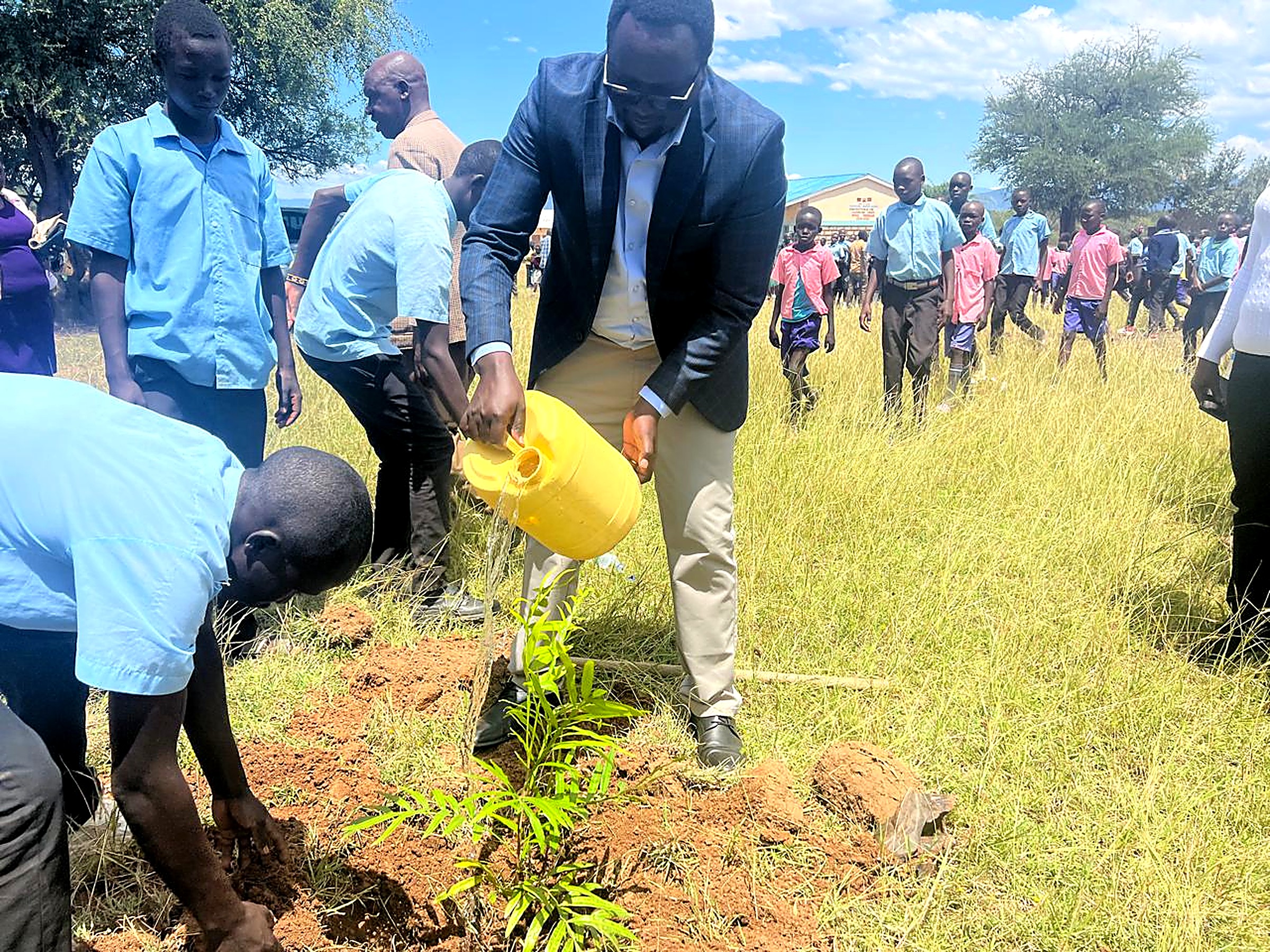 A leader and pupils watering a newly planted tree seedling at a school compound
